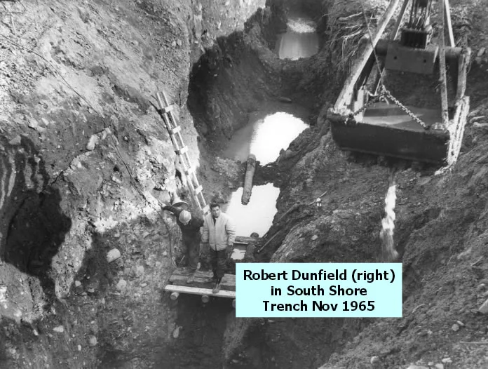 Men standing at the bottom of a deep, muddy trench beside a dragline crane.