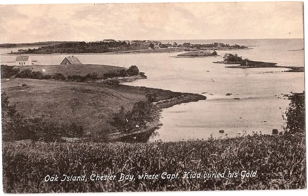 A sepia postcard looking across calm water to a low wooded island, with farm buildings on the near shore.