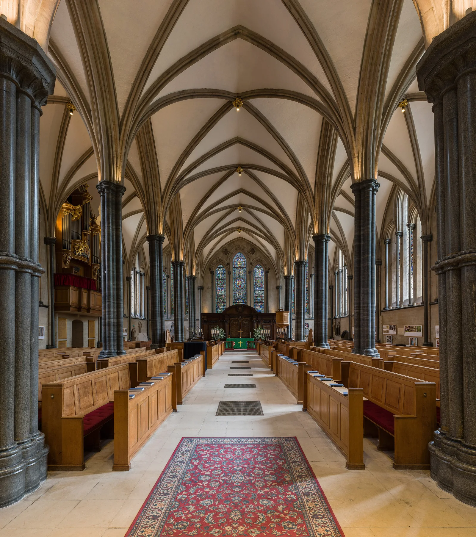 The interior of a medieval round church: a stone nave with pointed vaults, dark marble columns and rows of wooden pews leading to a stained-glass window.